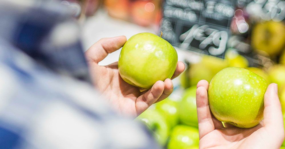 Ein Mann hält zwei frische grüne Äpfel in der Hand.